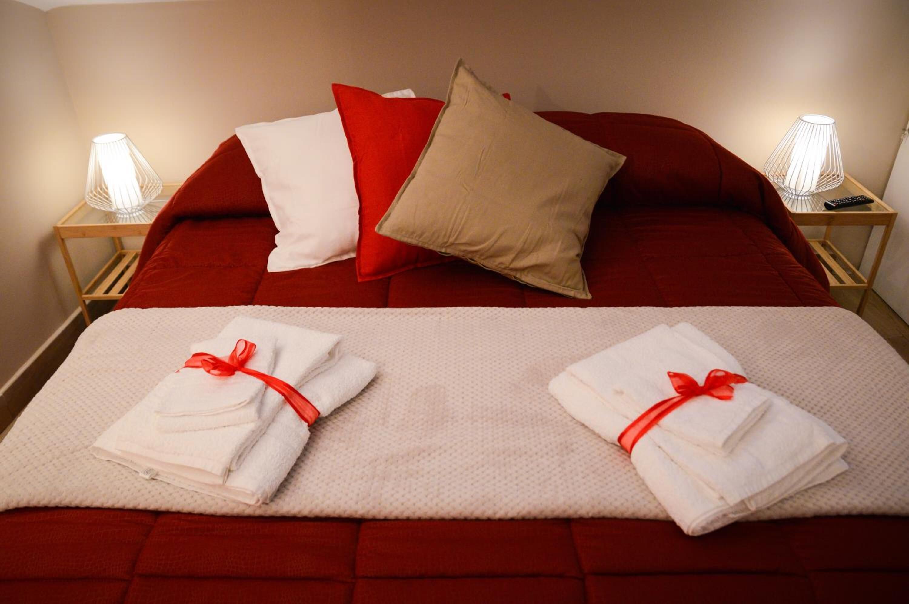Een opgemaakt bed met rode beddengoed, twee kussens en twee gevouwen handdoeken met rode linten.
