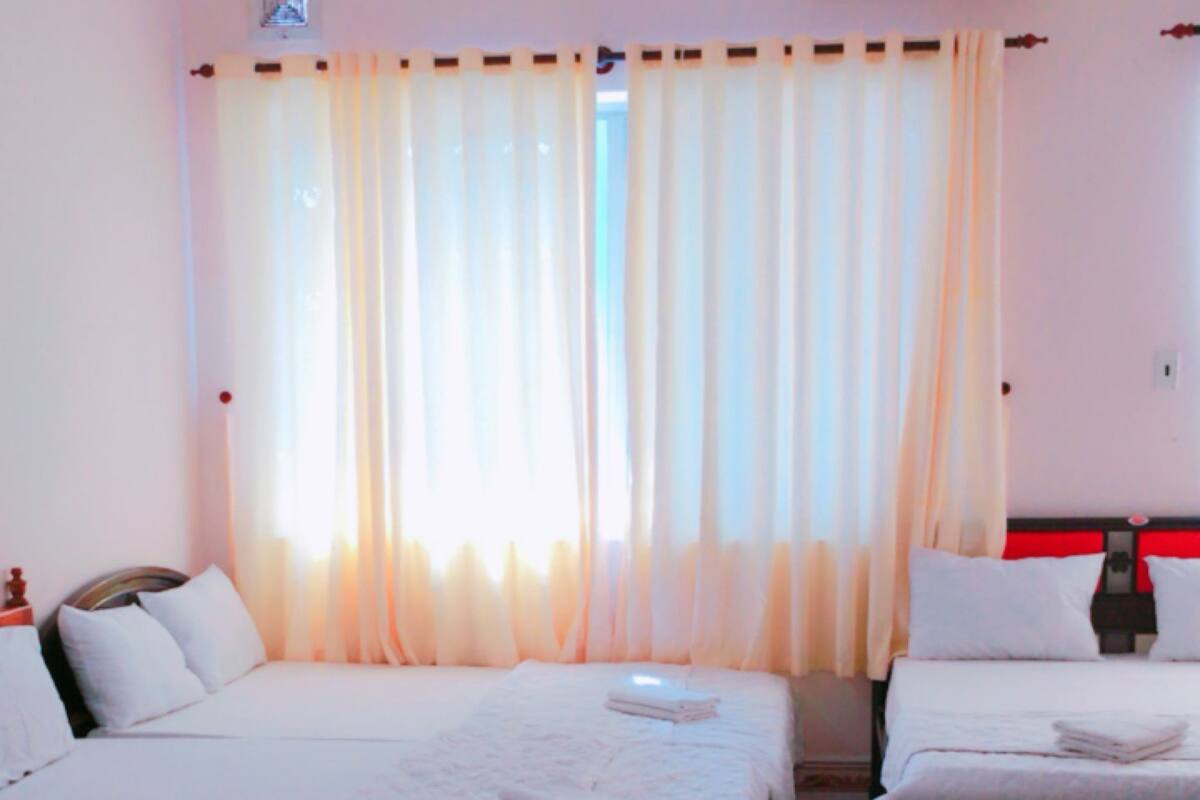 Habitación de hotel con dos camas, una ventana con cortinas, un equipo de aire acondicionado y suelo de baldosas.
