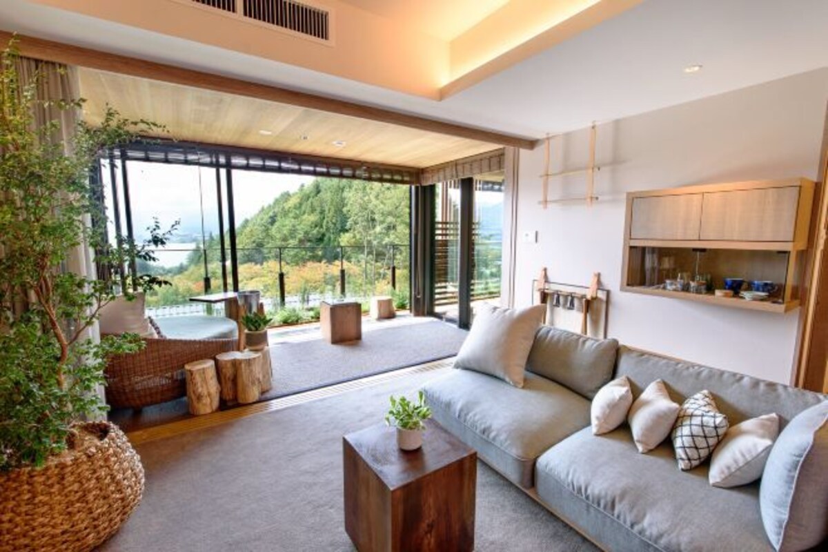 A modern living room with a large window, a sofa, a coffee table, and a potted plant.