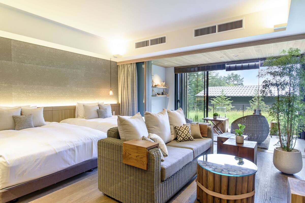 A modern hotel room with a large bed, a sofa, a small table, and a view of the outdoors.
