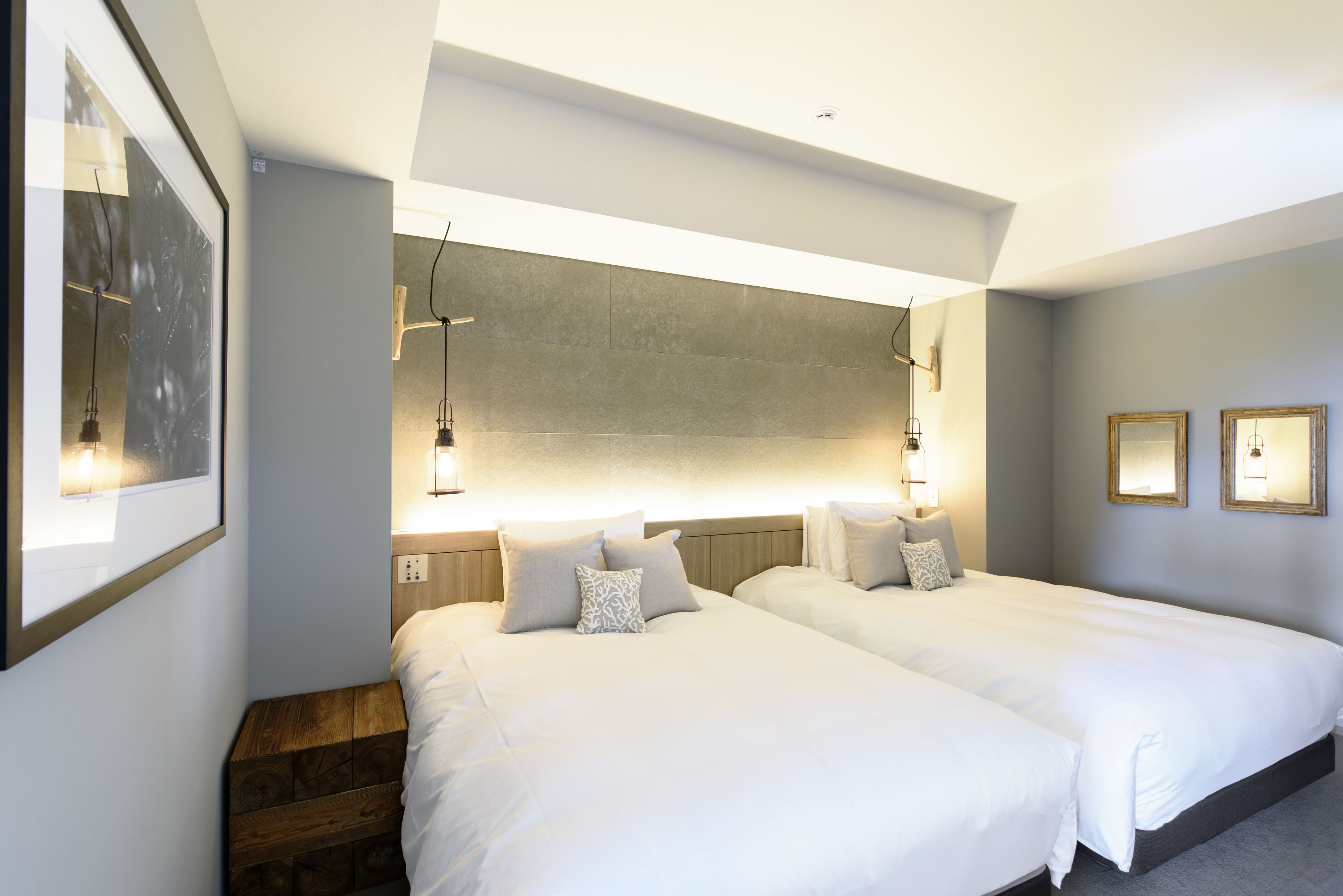 Habitación de hotel con dos camas, un banco de madera, un cuadro grande enmarcado e iluminación empotrada en la pared.