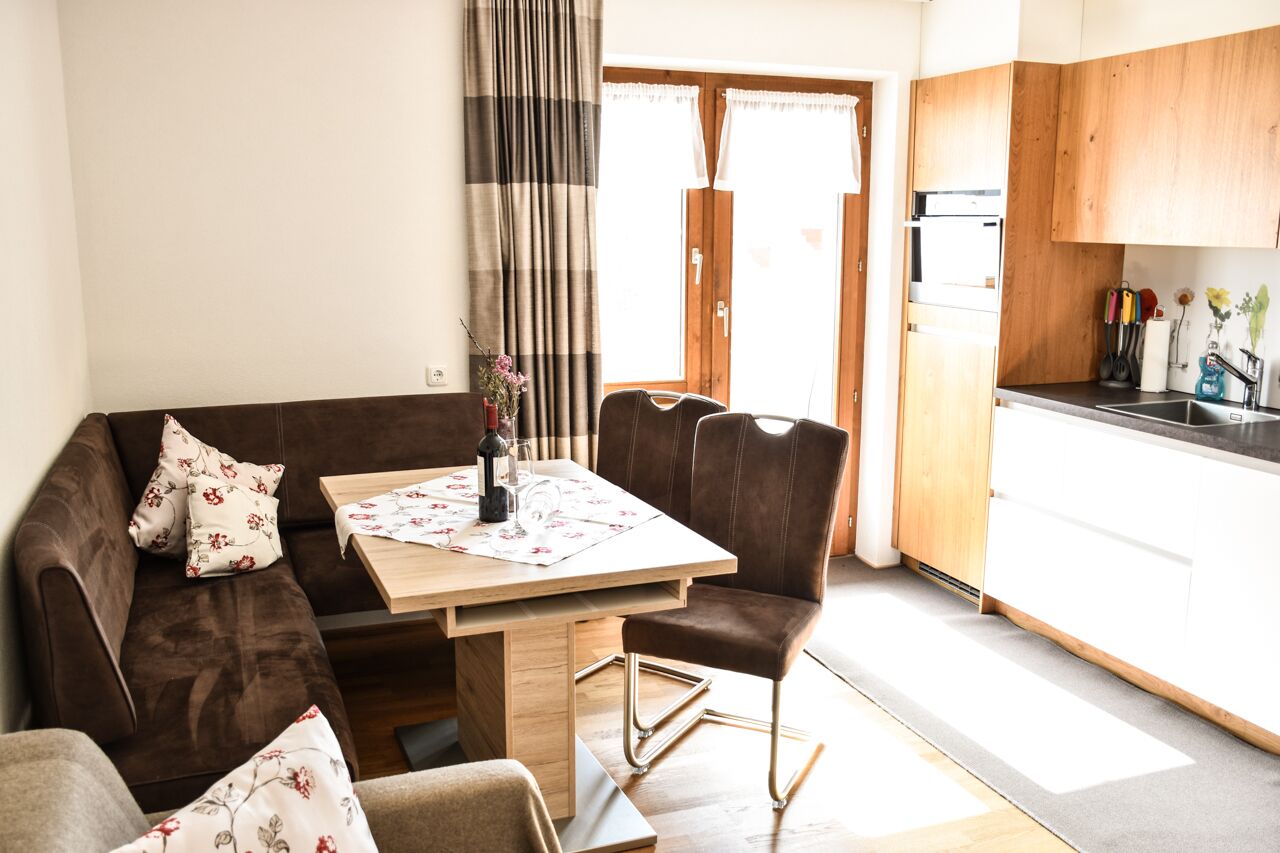 Una sala de estar acogedora con un sofá marrón, una mesa de comedor de madera y una cocina con armarios de madera y un lavabo.