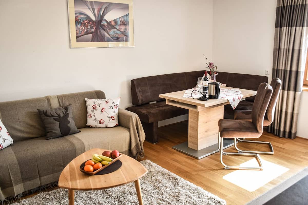 Una sala de estar moderna con un sofá marrón, una mesa de centro de madera con frutas, una mesa de comedor con sillas y un cuadro en la pared.