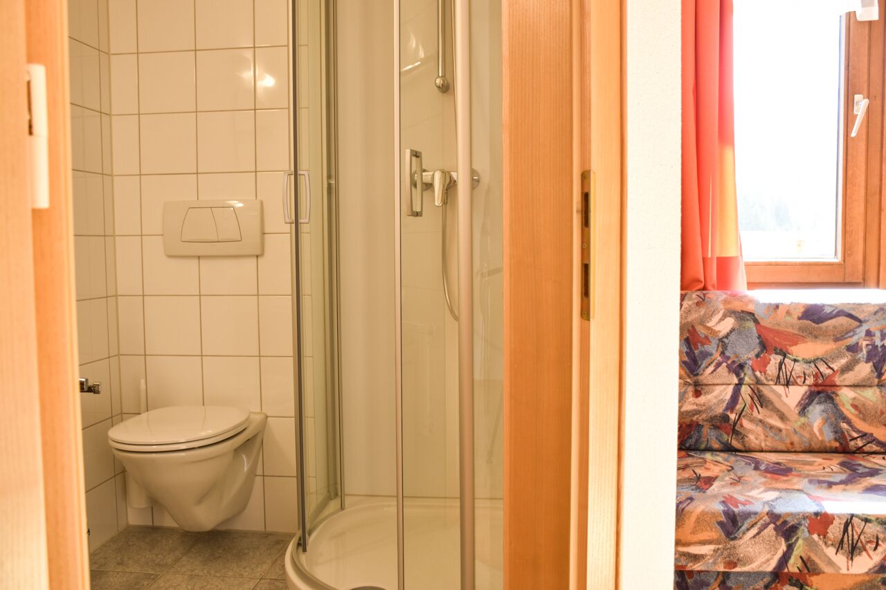 Een badkamer met een toilet, een douchecabine van glas en een raam met gordijnen.