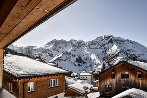 Een houten chalet met een met sneeuw bedekte dak, tegen een achtergrond van besneeuwde bergen.