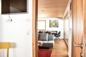 Een moderne woonkamer met een grijze bank, een houten plafond en een eethoek met een tafel en stoelen.