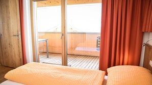 Un dormitorio con piso de madera, una cama con manta amarilla, un cerrojo corredizo que da a un espacio al aire libre y una cortina roja.