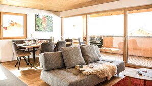 Una sala moderna con un sofá gris, piso de madera y un comedor con sillas y una mesa.