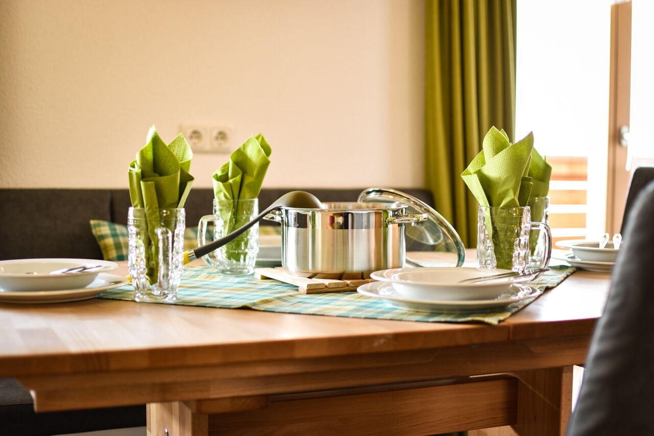 A dining table set with clear glassware, green napkins, and a stainless steel pot.