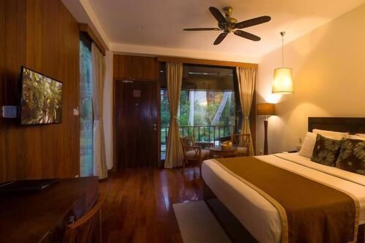 A hotel room with a bed, a desk, a chair, a ceiling fan, and a window with curtains.