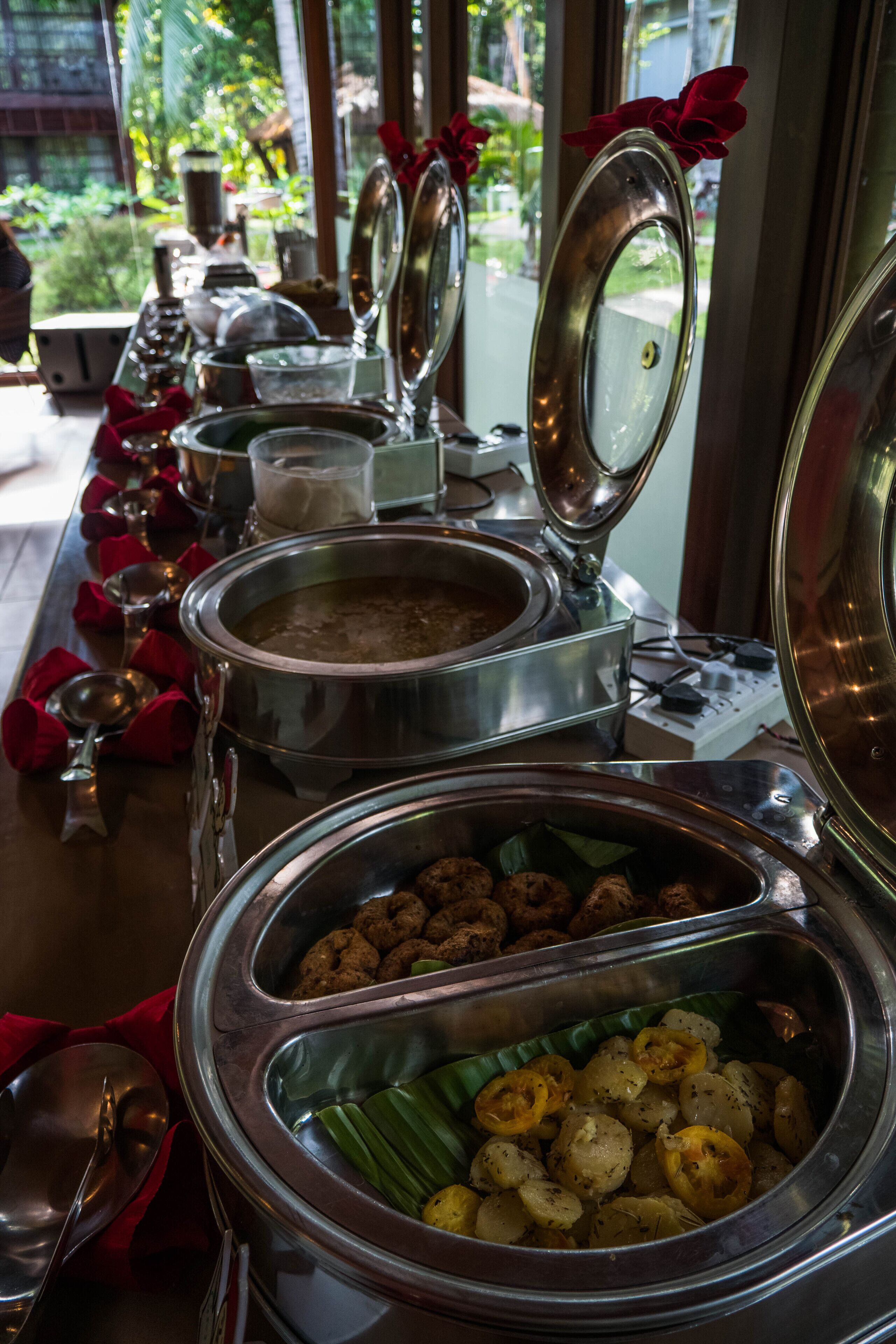 A buffet setup with various food items in metal containers, some with lids open.