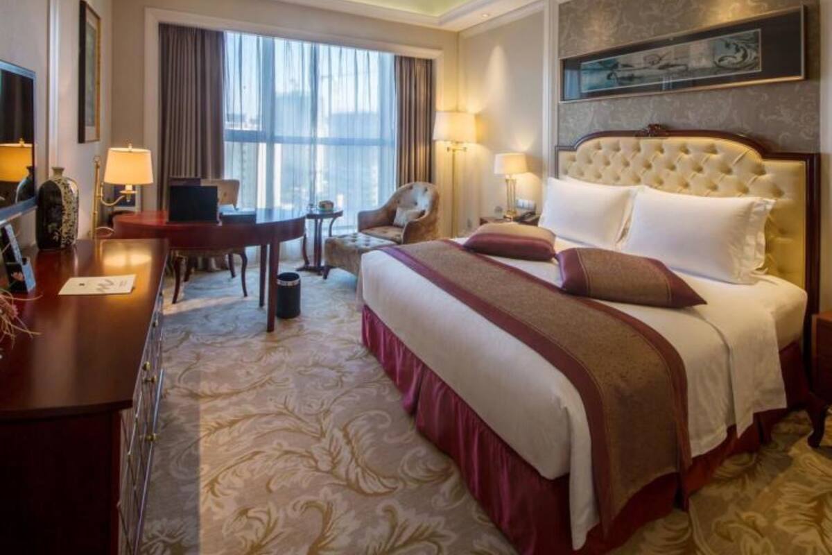 A hotel room with a large bed, a desk, a chair, and a window with curtains.