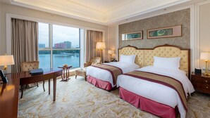 A hotel room with two beds, a desk, and a chair. There are two lamps on the nightstands and a view of a river and buildings through the window. - Grand Metropark Guofeng Hotel Tangshan (Tangshan)