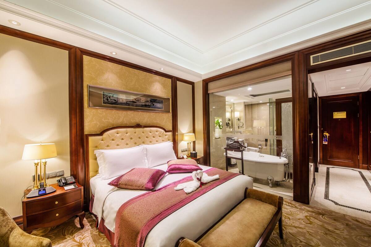 A hotel room with a large bed, bedside tables, a mirror, and a bathroom visible through an open door.