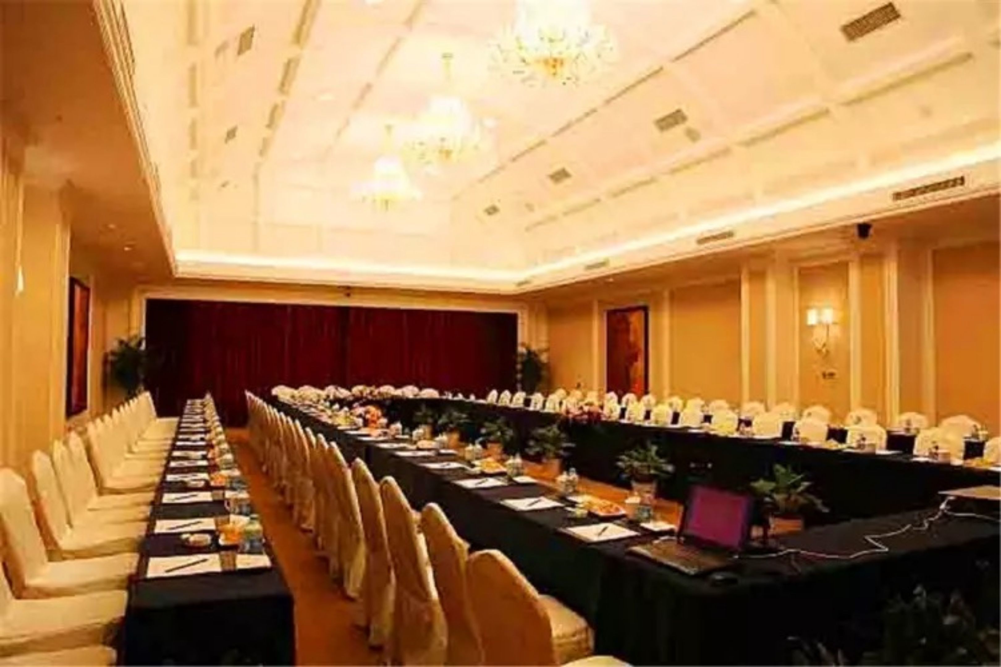 A long conference table with chairs, a stage, and chandeliers.