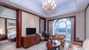 A hotel room with a large bed, a TV, a desk with a laptop, a sofa, and a large window with a view of the city. - Grand Metropark Guofeng Hotel Tangshan (Tangshan)