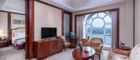 A hotel room with a large bed, a TV, a desk with a laptop, a sofa, and a large window with a view of the city.