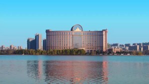 A large, rectangular building with a central dome and multiple windows, situated by a body of water with reflections. - Grand Metropark Guofeng Hotel Tangshan (Tangshan)
