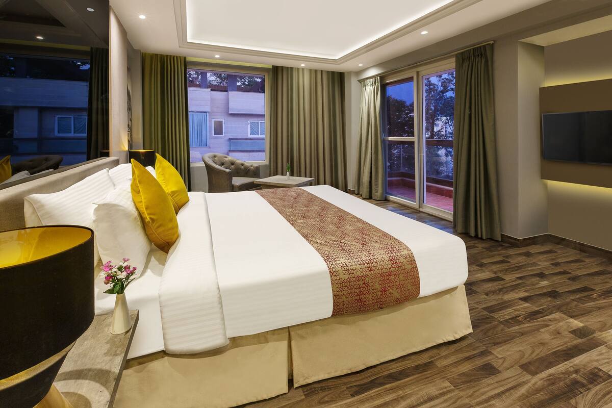 A modern hotel room with a large bed, a sofa, a TV, and a balcony with curtains.