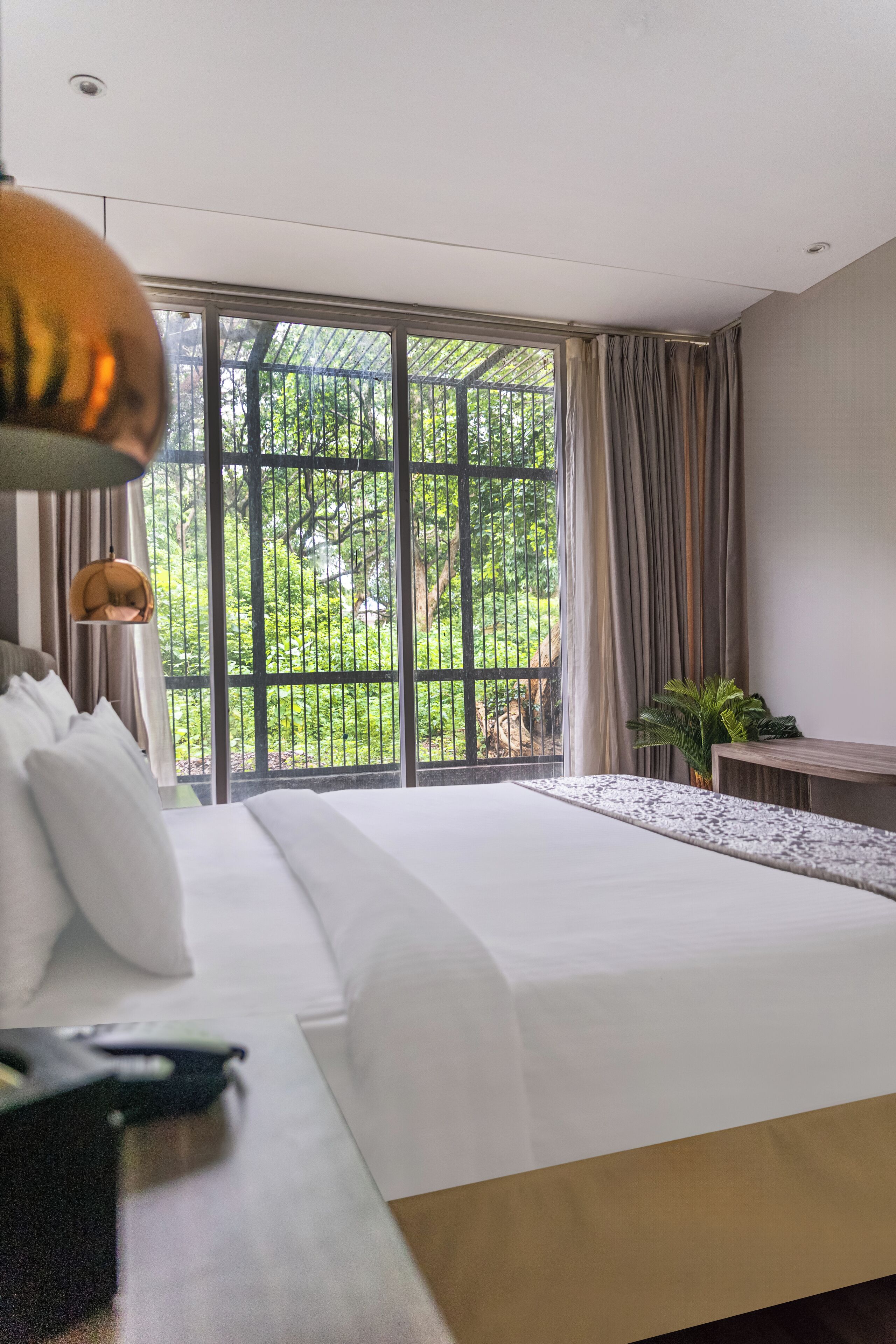 A modern bedroom with a large window, a bed, a bedside table, and a hanging light fixture.