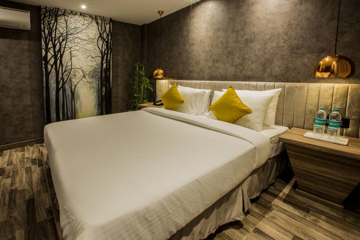 A modern hotel room with a large bed, a nightstand, a wall-mounted lamp, and a water bottle on the nightstand.