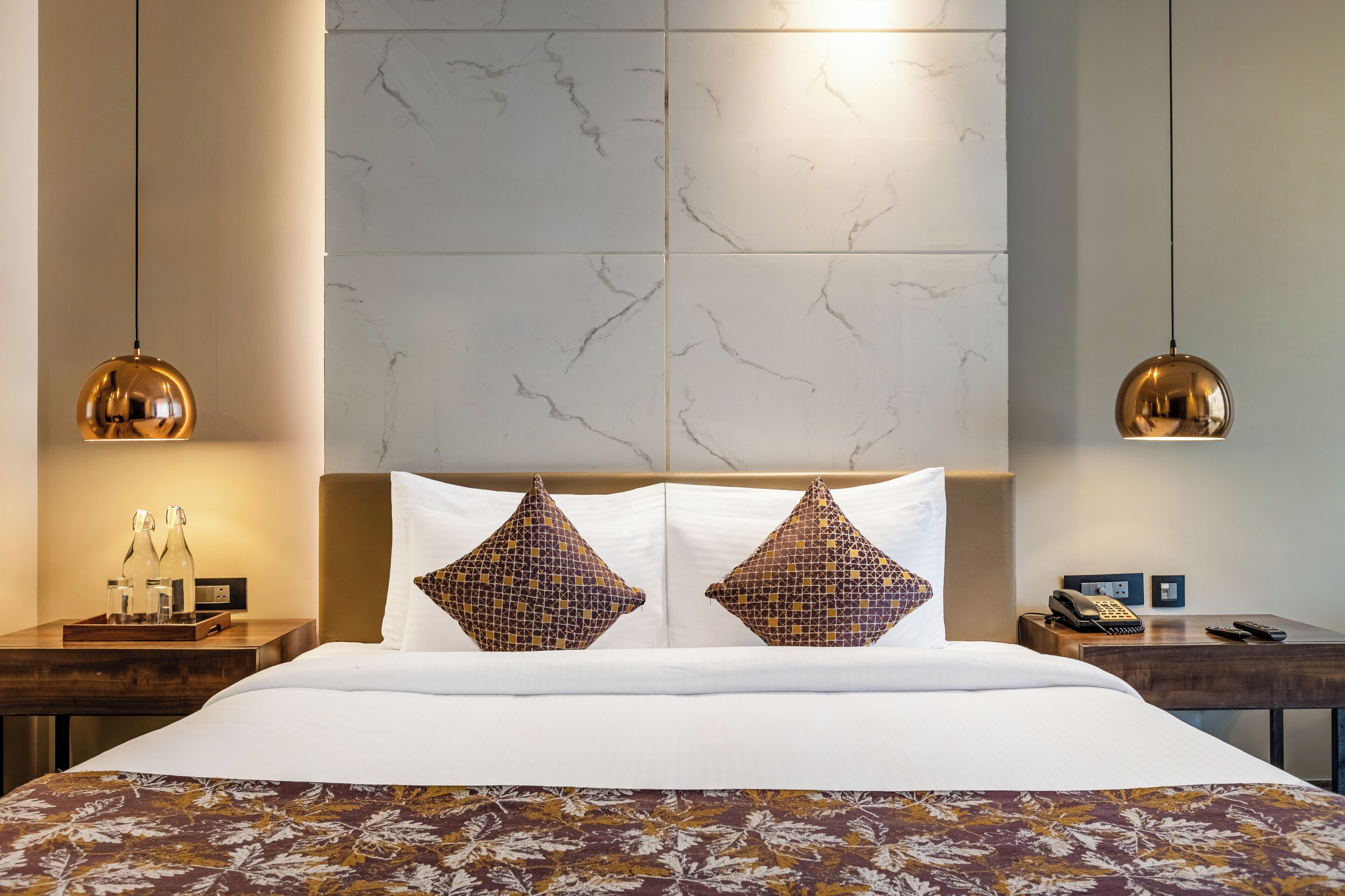 Hotelkamer met een groot bed, twee gestreepte kussens, een houten nachtkastje met telefoon en een marmeren wand.