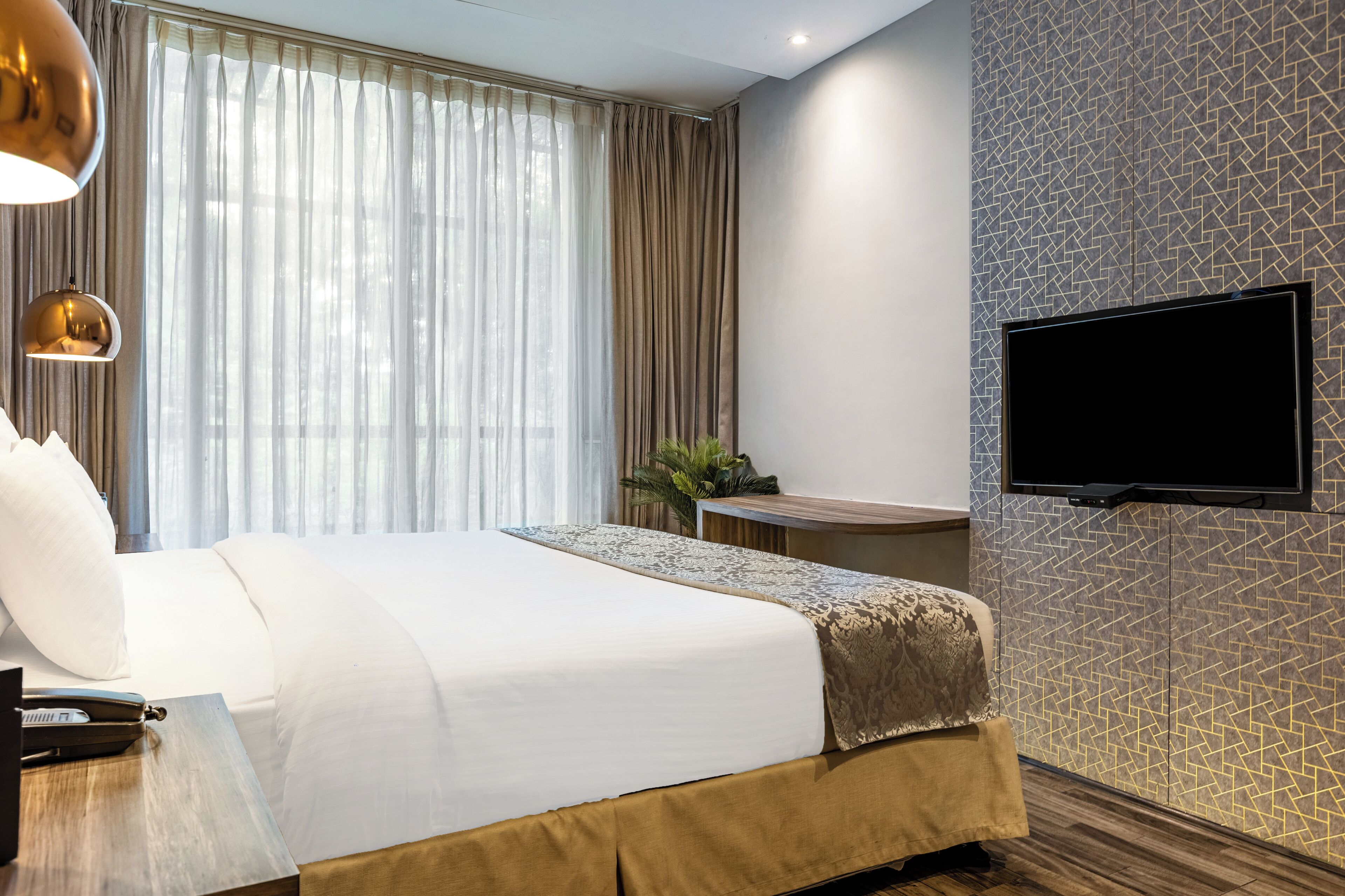 A modern hotel room with a large bed, a flat-screen TV mounted on the wall, and a window with sheer curtains.