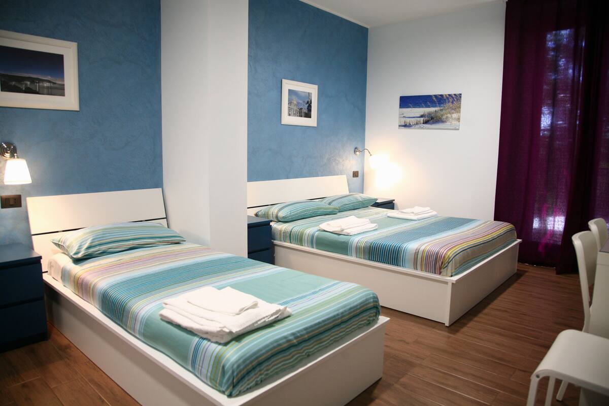 A hotel room with two single beds, a desk, and a chair.