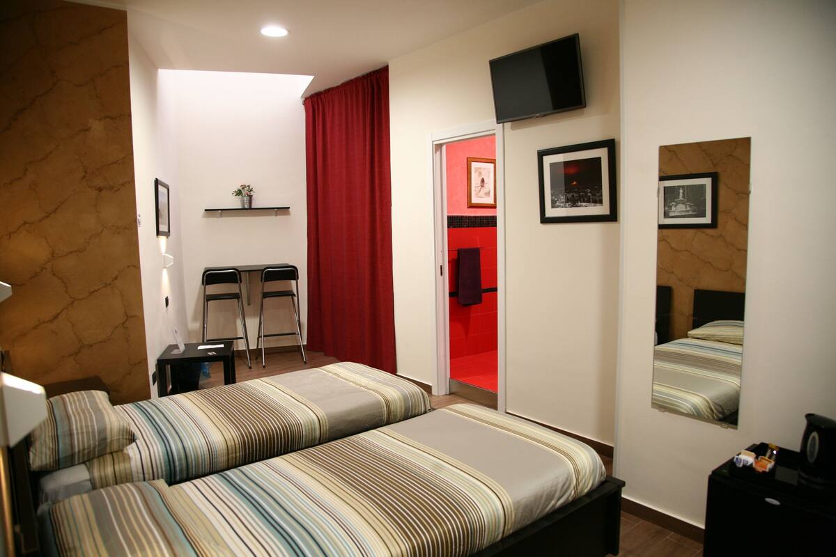 A hotel room with two beds, a TV, a red curtain, and framed pictures on the wall.