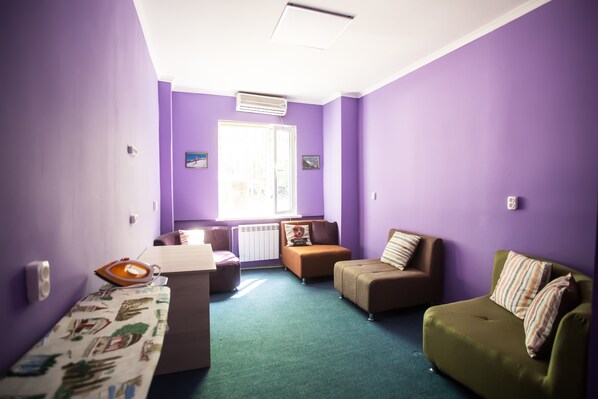 A room with purple walls, a green carpet, a sofa, a small table, and a window with natural light.