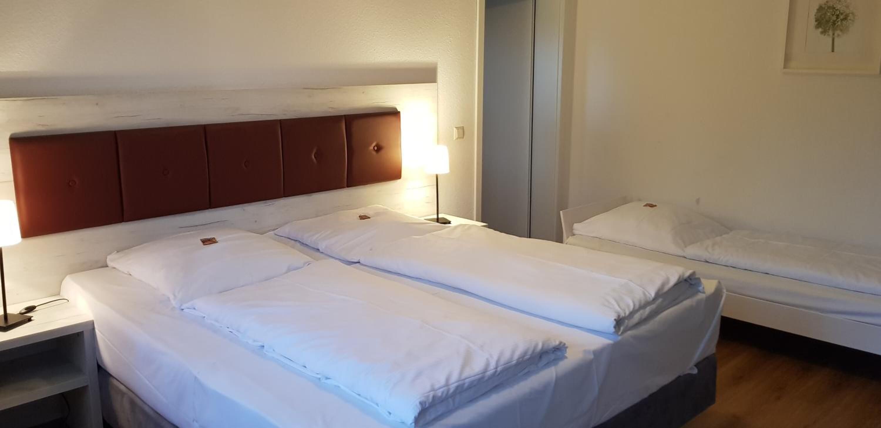 Une chambre d’hôtel avec deux lits, une tête de lit en bois, une lampe de chevet et un tableau encadré au mur.