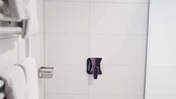 Un baño con paredes de azulejos blancos, zona de ducha y un perchero con toallas.