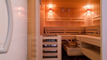 A sauna with wooden benches, a bench with a tray, and two wall-mounted light fixtures.