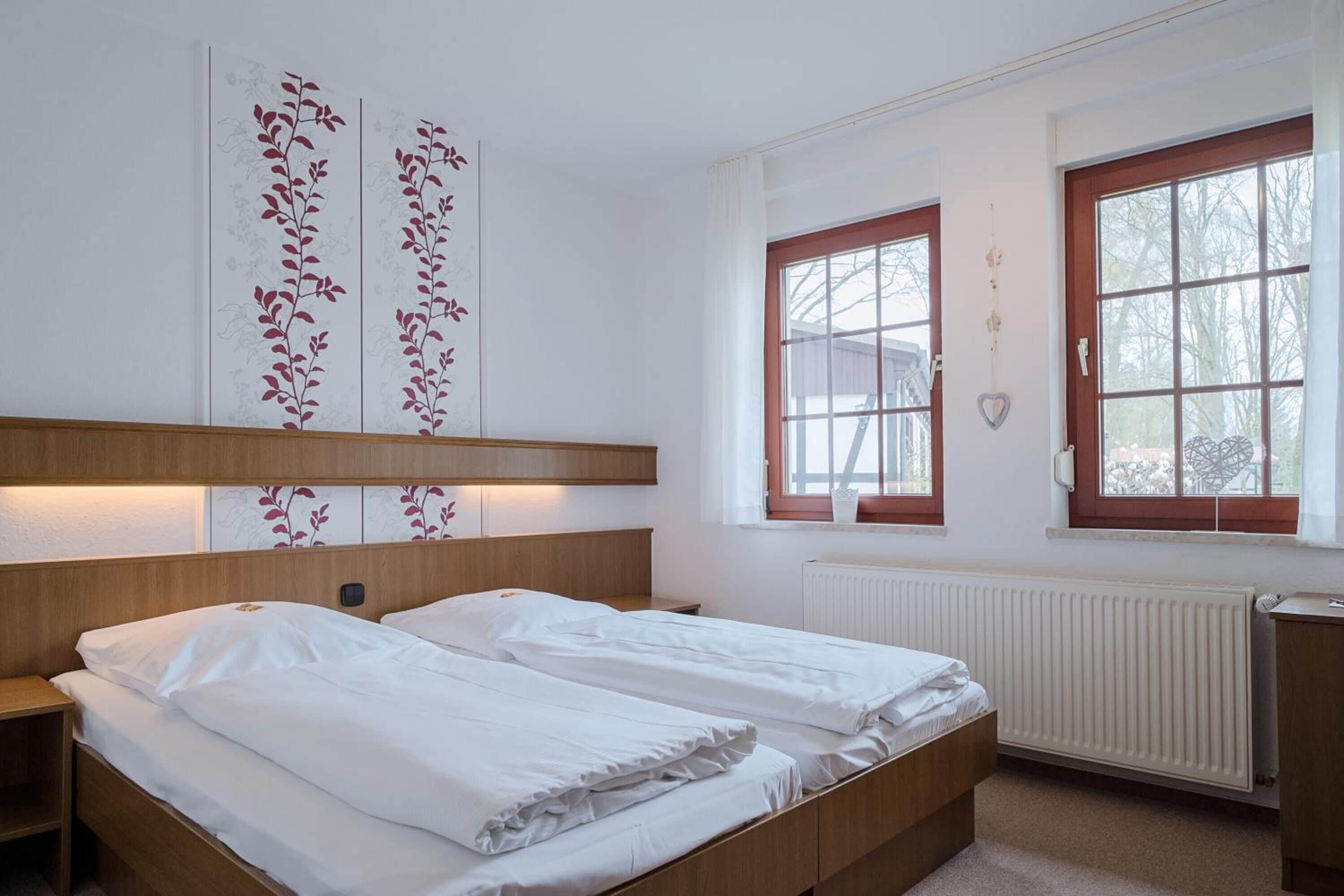 A hotel room with two beds, a wooden headboard, a radiator, and a window with a view of trees.