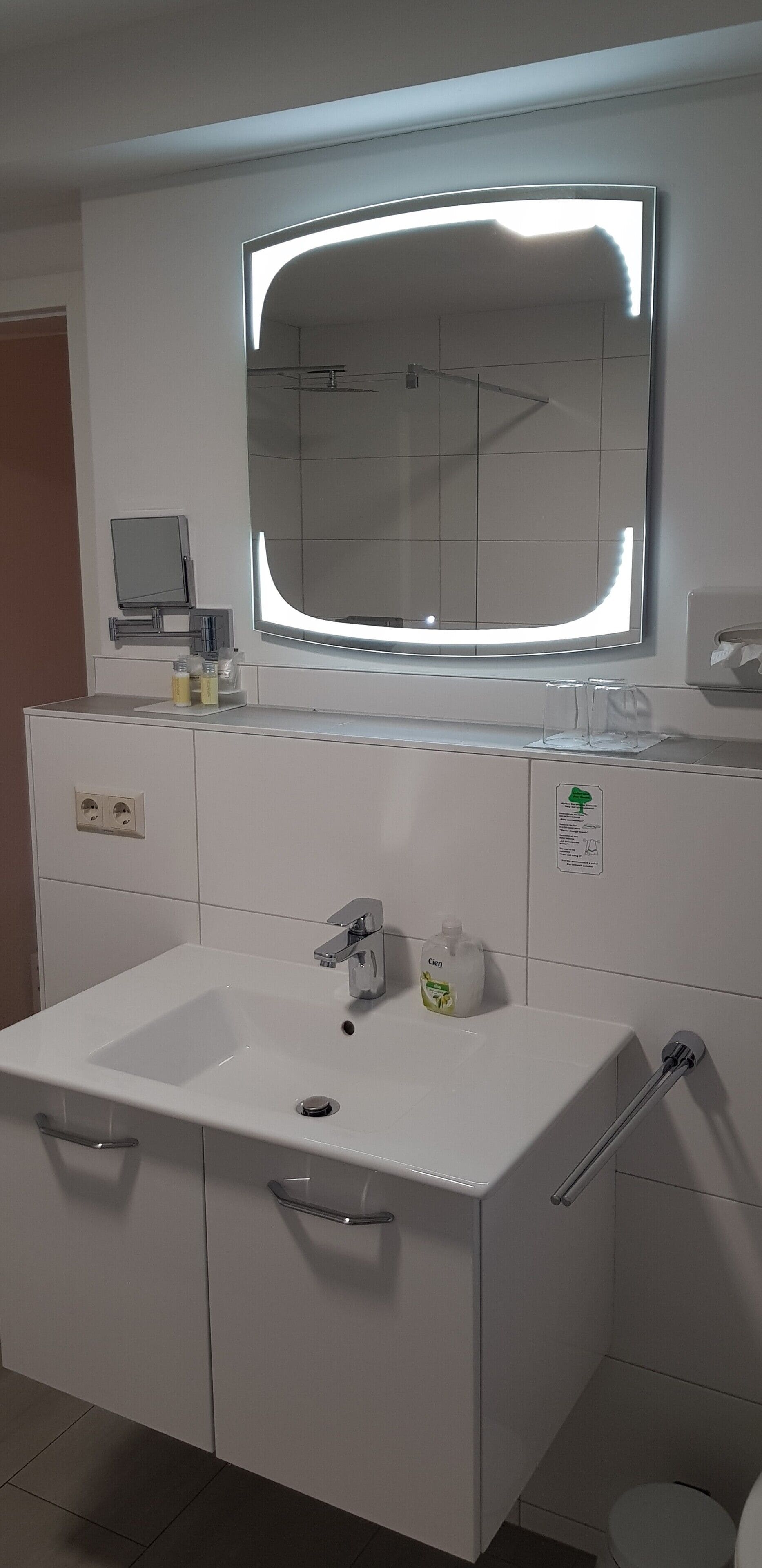 Ein modernes Badezimmer mit einem großen Spiegel, einem weißen Waschbecken und einer Toilette.