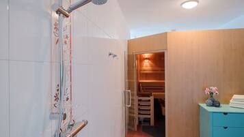 Bathroom features a glass-enclosed shower, handheld showerhead, and a wooden vanity with a small vase.