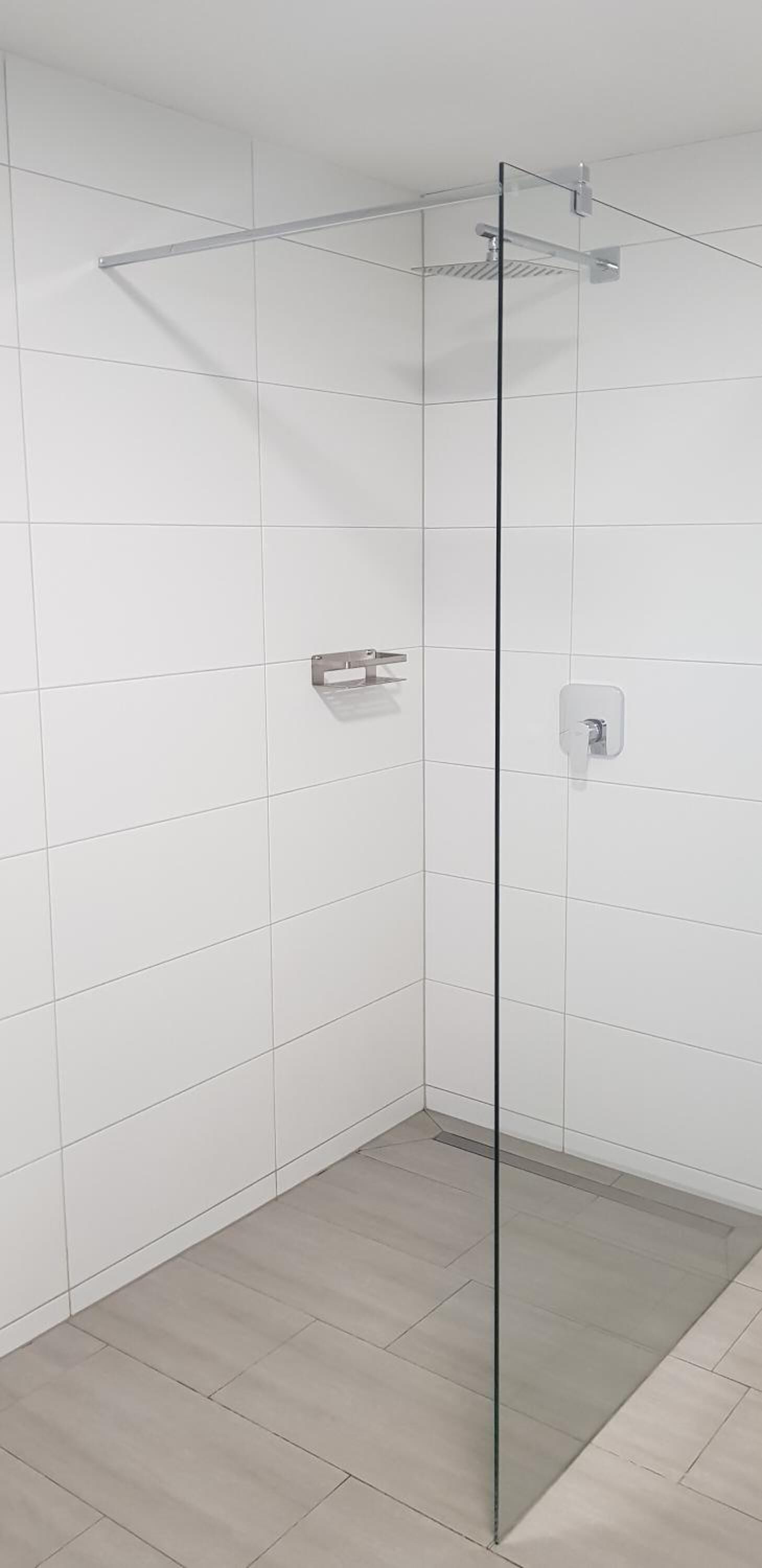 A modern shower with a glass door, white tiled walls, and a light-colored floor.