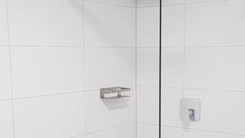 A modern shower with a glass door, white tiled walls, and a light-colored floor.