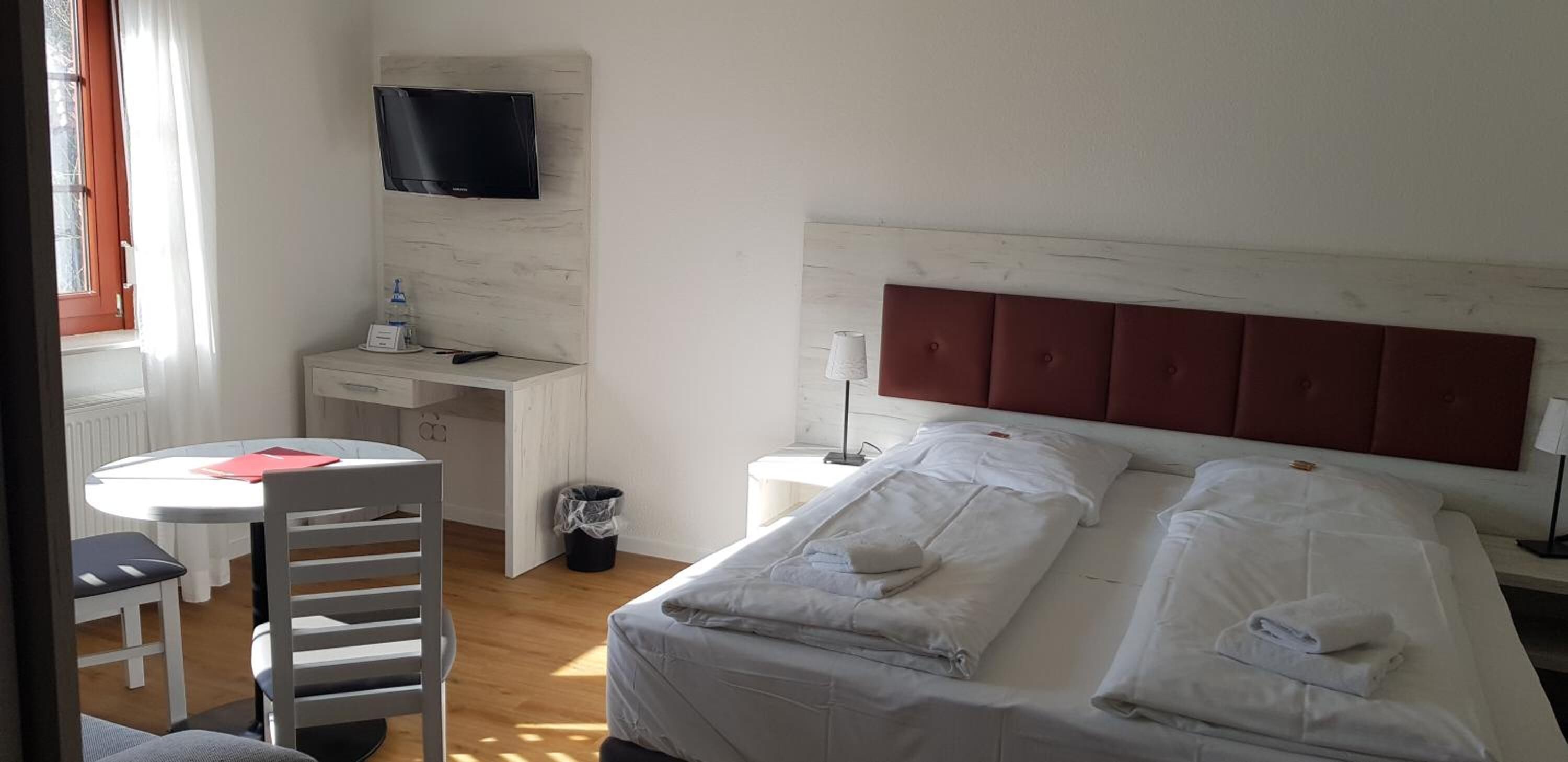 Habitación de hotel con cama, escritorio, silla, televisor y ventana.