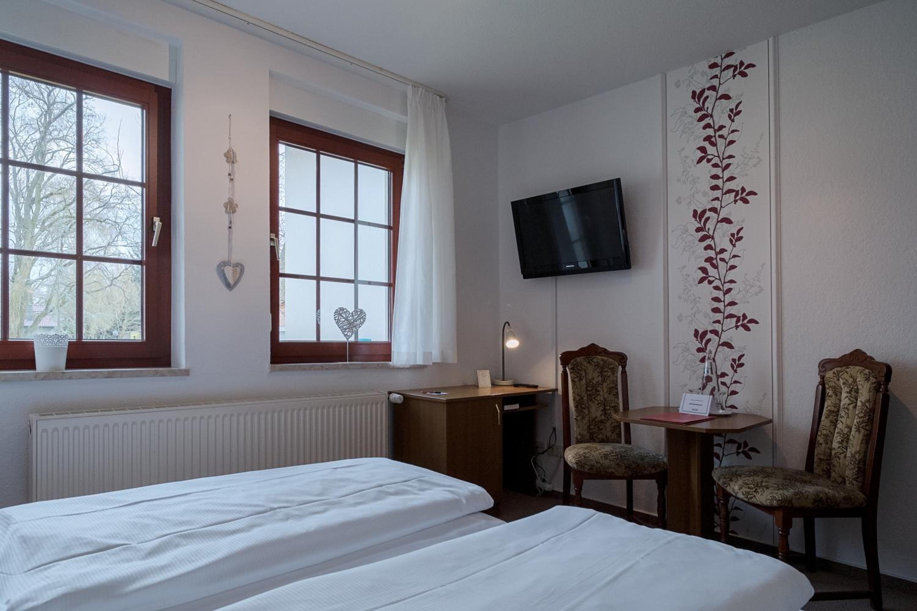Une chambre d’hôtel avec deux lits, un bureau, deux chaises, une télévision et une fenêtre donnant sur des arbres.