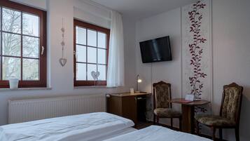 Quarto de hotel com duas camas, uma escrivaninha, duas cadeiras, uma televisão e uma janela com vista para árvores.