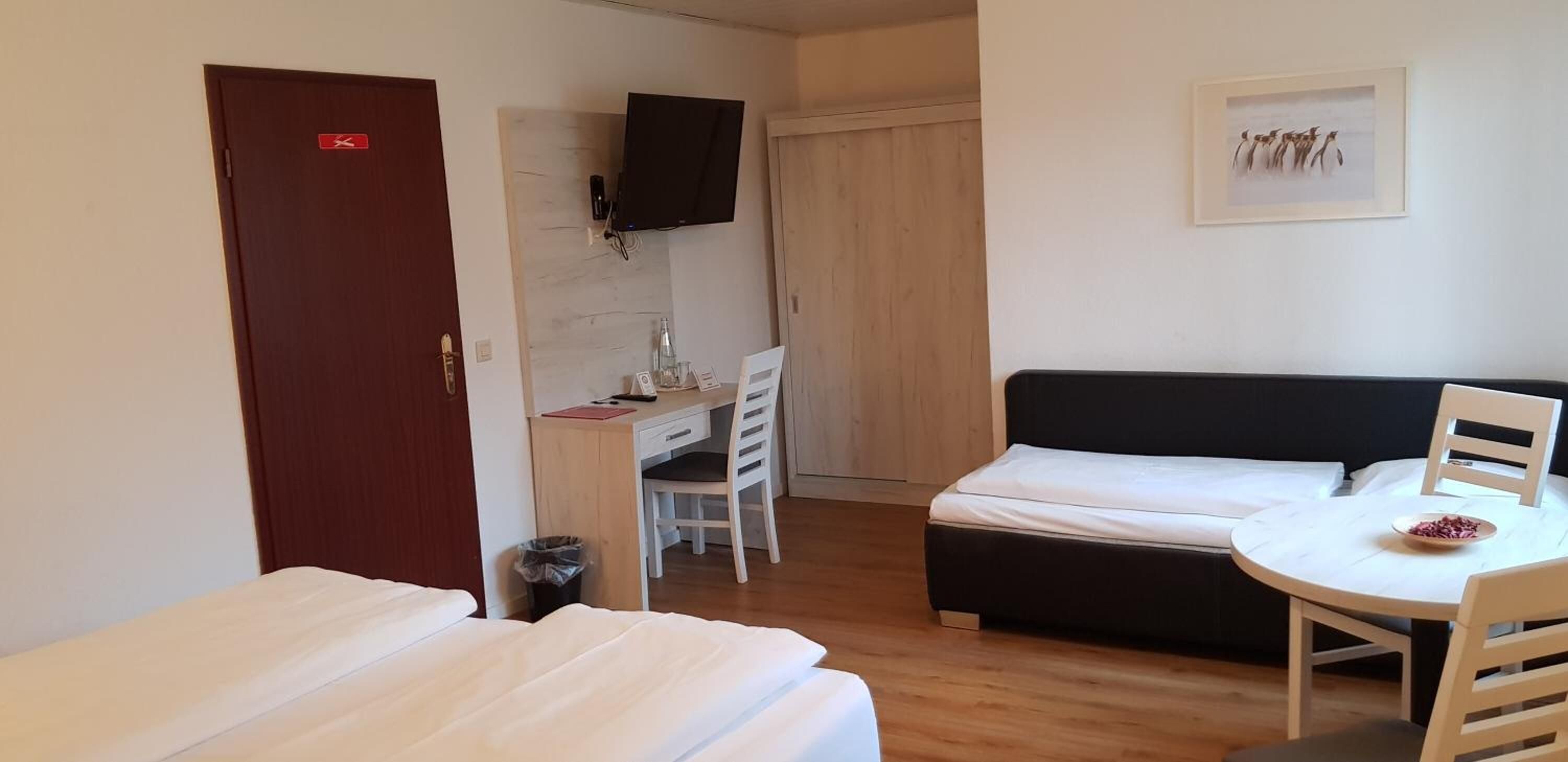 Ein Hotelzimmer mit Bett, Schreibtisch mit Stuhl, Wandfernseher und einem gerahmten Bild an der Wand.