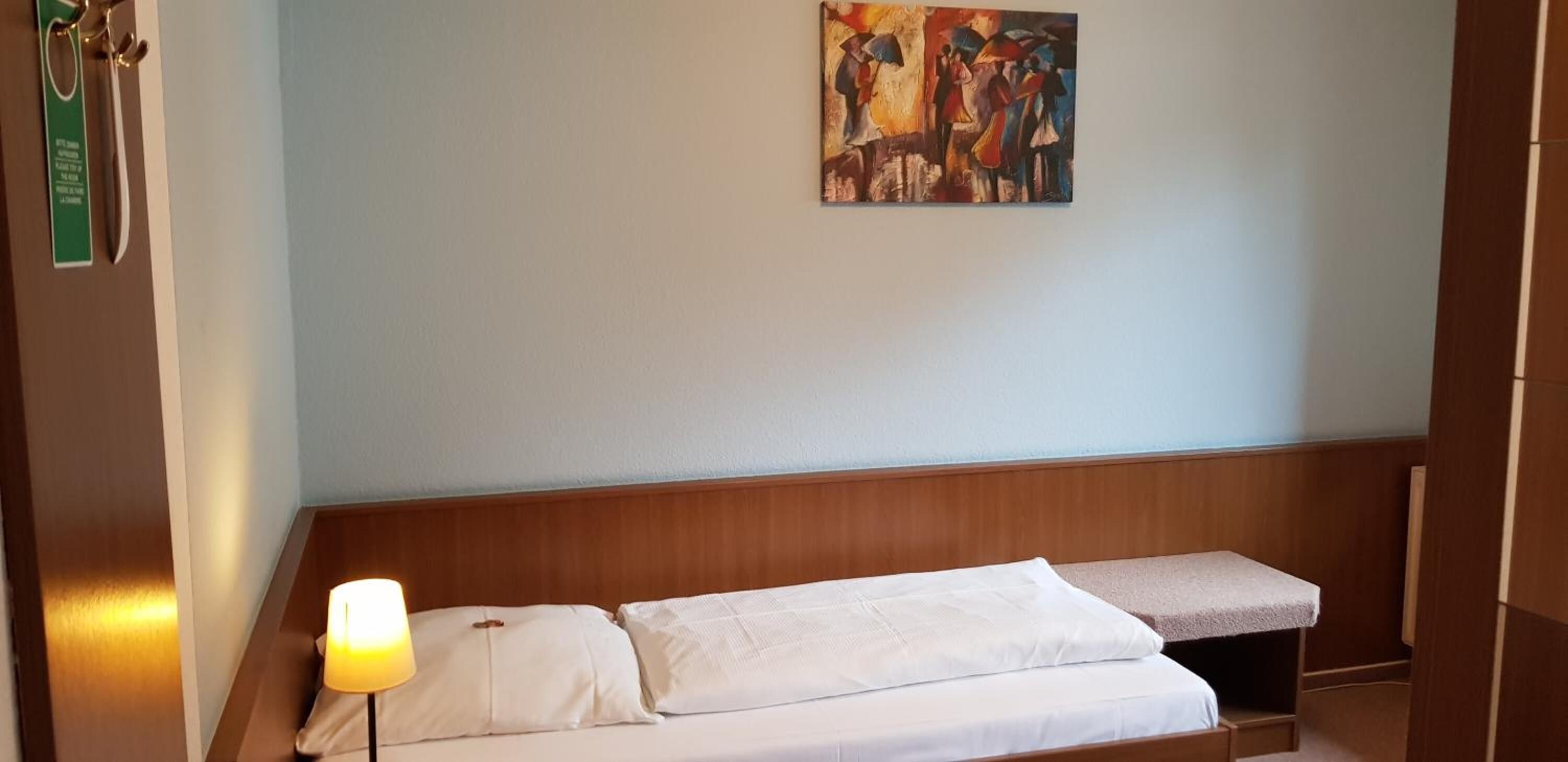 A hotel room with a bed, a bedside lamp, a painting on the wall, and a wooden headboard.