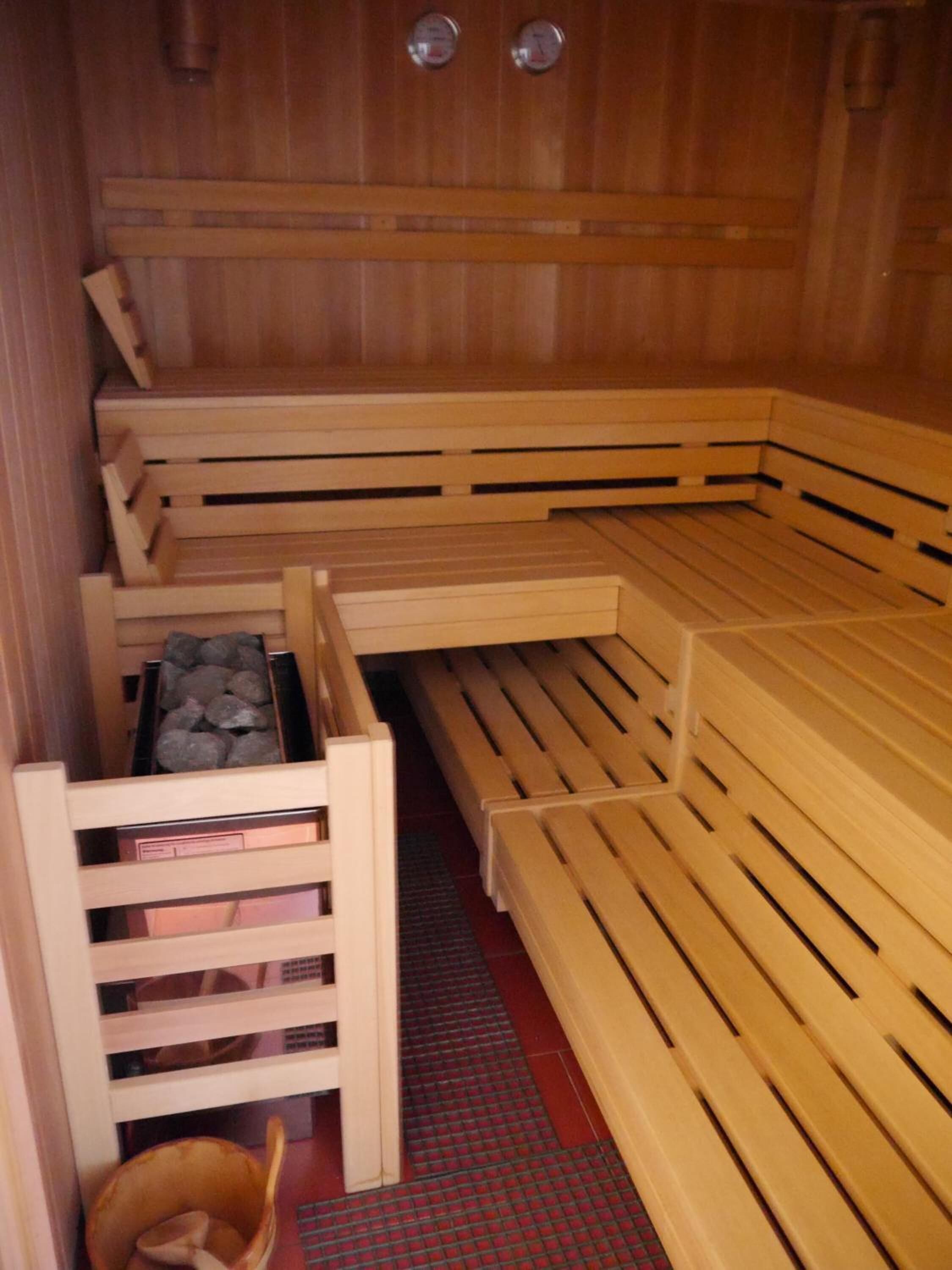 A sauna with wooden benches, a bench with a storage compartment, and a small wooden bucket.