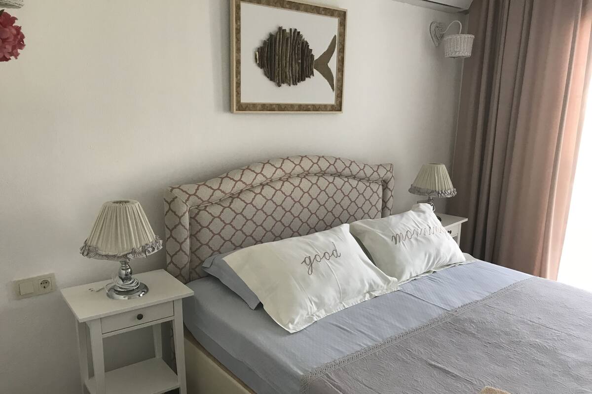 Une chambre à coucher bien rangée, avec une tête de lit à motifs, une table de chevet avec une lampe et des coussins ornés de motifs textuels.