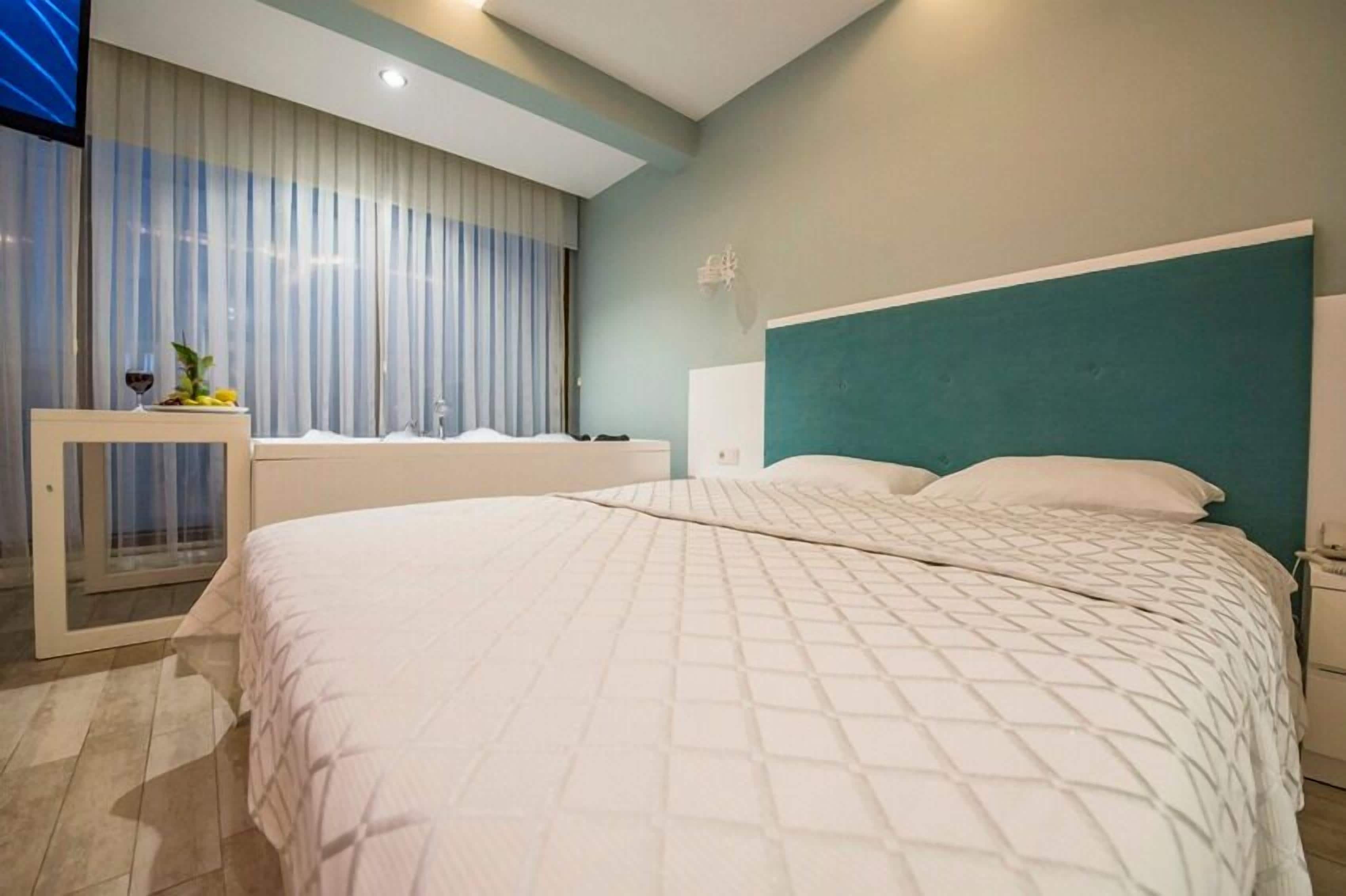 Una habitación de hotel moderna con una cama grande, una mesita con una copa de vino y fruta, y un televisor en la pared.