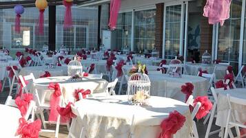 Un espacio para eventos al aire libre con mesas redondas cubiertas con manteles blancos, decorado con flores rojas y sillas blancas.