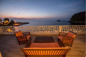 A balcony with wicker furniture and a view of the sea at dusk.