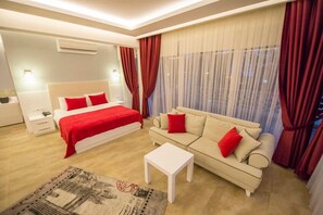 A modern hotel room with a bed, a sofa, a small table, and a large window with curtains.