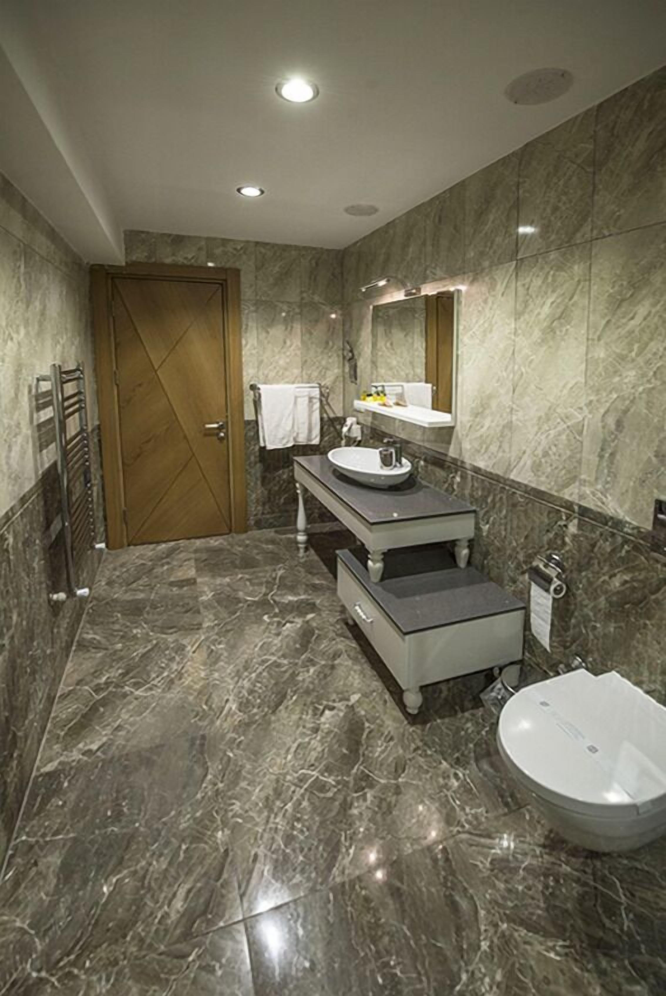 Une salle de bain moderne avec un sol en marbre, un meuble-lavabo à deux vasques, des toilettes et un porte-serviettes.